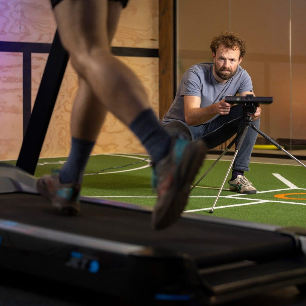 Een hardloper die een 3D hardloopanalyse ondergaat, in de achtergrond staat een man met een camera